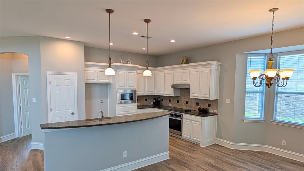 Kitchen featuring white shaker-style cabinetry, dark stone countertops, stainless steel appliances, pendant lighting, and wood-finish flooring