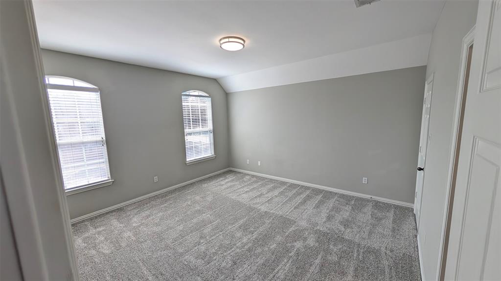 Neutral-toned interior featuring plush carpeting, vaulted ceilings, and two arched windows