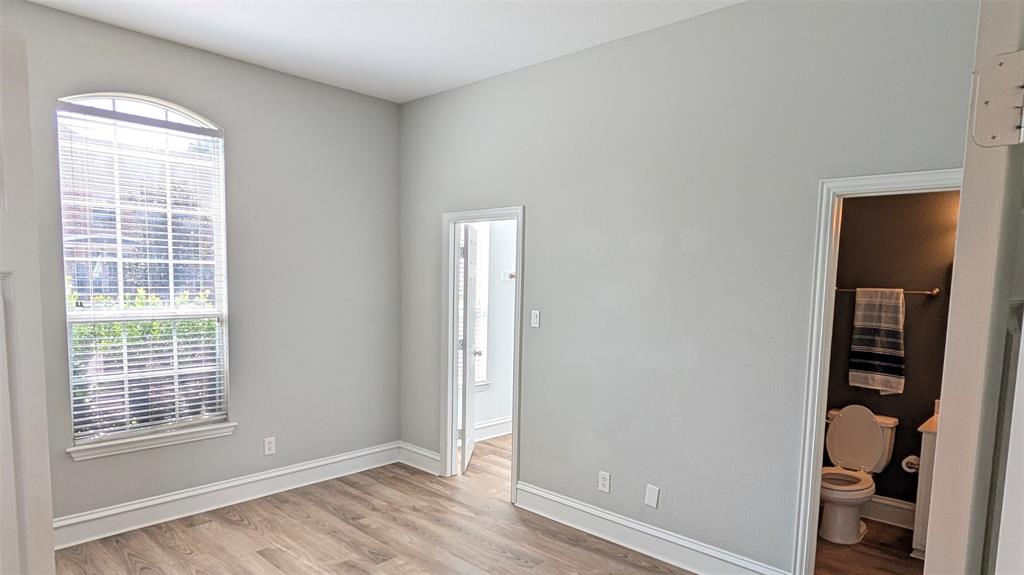 Room featuring an arched window, wood-finish flooring, and neutral wall tones