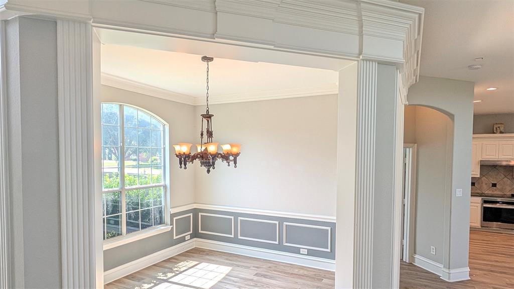 Arched window with grid detailing, decorative wainscoting, crown molding, fluted column framing, and multi-bulb metal chandelier