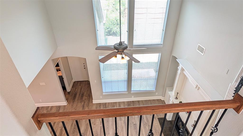 Double-height ceiling, floor-to-ceiling windows, built-in fireplace mantle, wood-finish flooring, and staircase with a wood-finished handrail and metal balusters