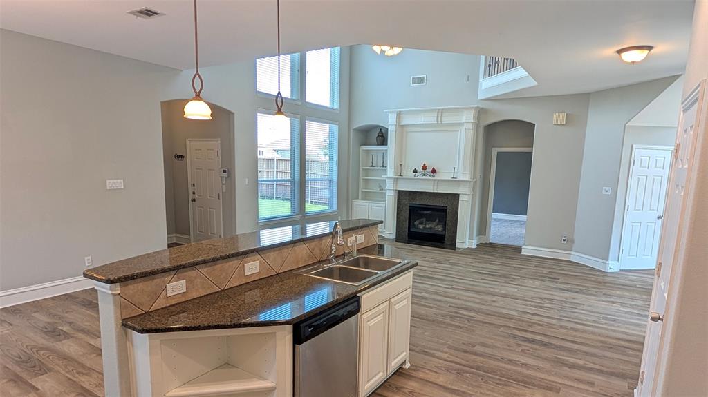 Kitchen island with stone countertop and dual-basin stainless steel sink, wood-finish flooring, two-story windows, and fireplace with decorative mantel and built-in shelving
