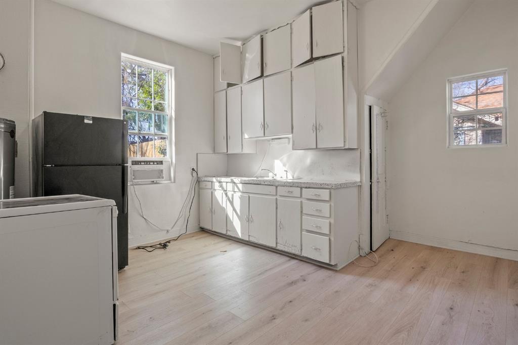 Kitchen featuring wood-finish flooring, white cabinetry with extended upper storage, speckled-surface countertops, and dual windows Kitchen featuring wood-finish flooring, white cabinetry with extended upper storage, speckled-surface countertops, and dual windows