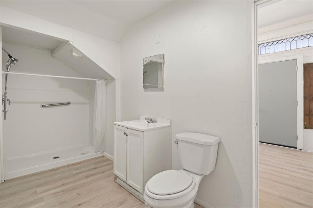 Bathroom featuring wood-finish flooring, a white vanity with a single-basin countertop, a wall-mounted medicine cabinet, and a walk-in shower stall with a grab bar Bathroom featuring wood-finish flooring, a white vanity with a single-basin countertop, a wall-mounted medicine cabinet, and a walk-in shower stall with a grab bar