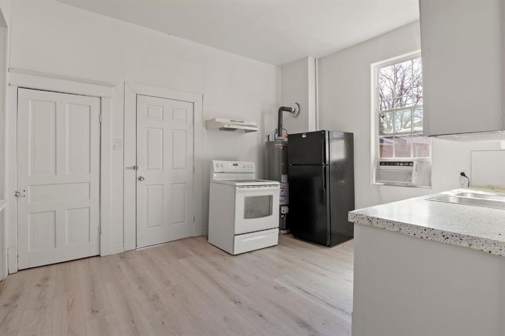 Kitchen area featuring wood-finish flooring, two white paneled doors, light-toned countertop, and window Kitchen area featuring wood-finish flooring, two white paneled doors, light-toned countertop, and window