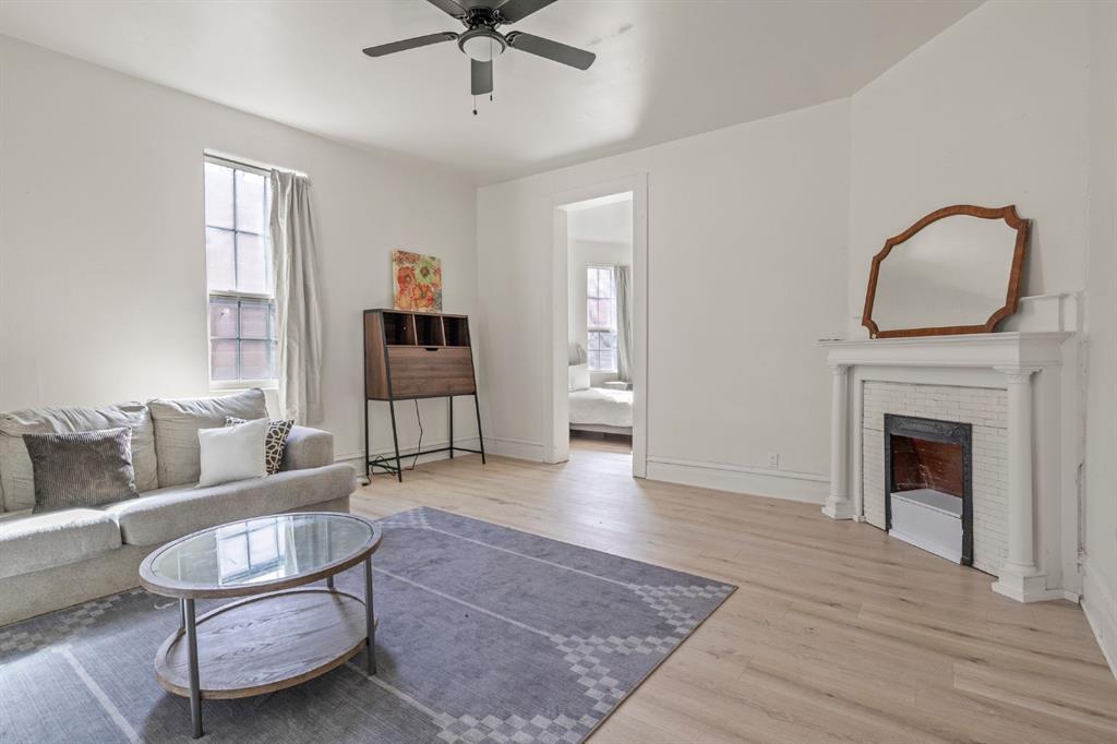Light-filled living area featuring wood-finish flooring, a white mantel fireplace with tile surround, and a ceiling fan Light-filled living area featuring wood-finish flooring, a white mantel fireplace with tile surround, and a ceiling fan