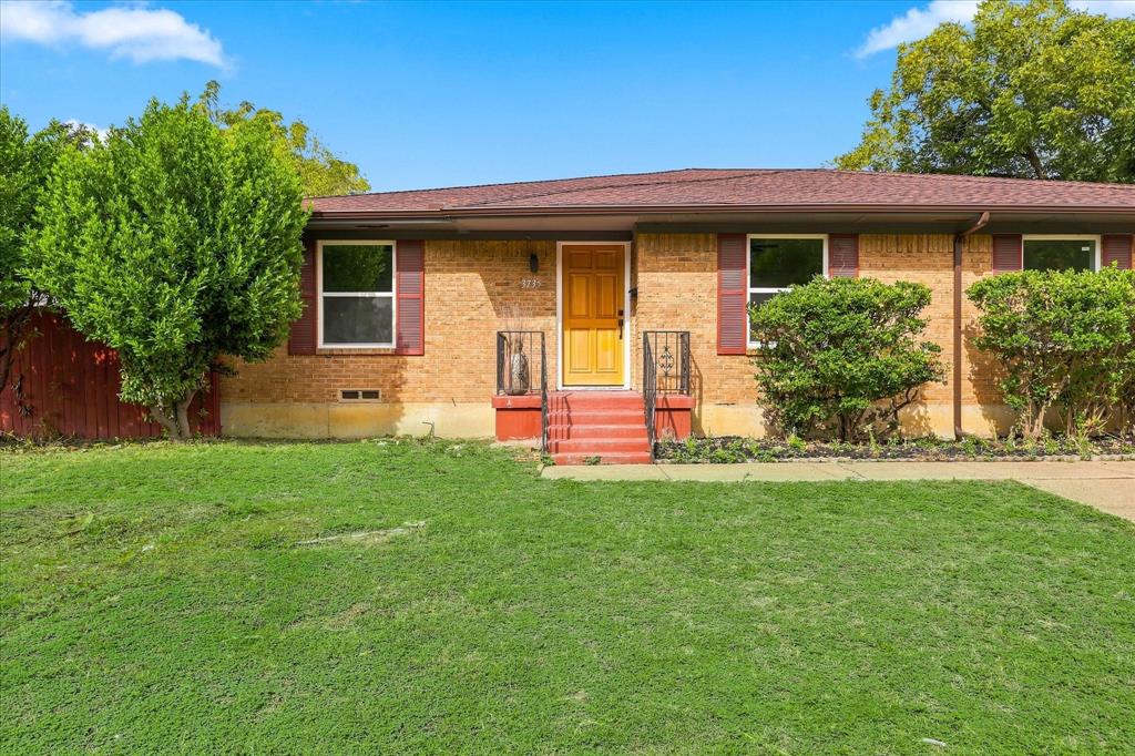 Single-story brick exterior featuring dark shutter accents, a wood-finish front door, metal handrails, and a wide lawn