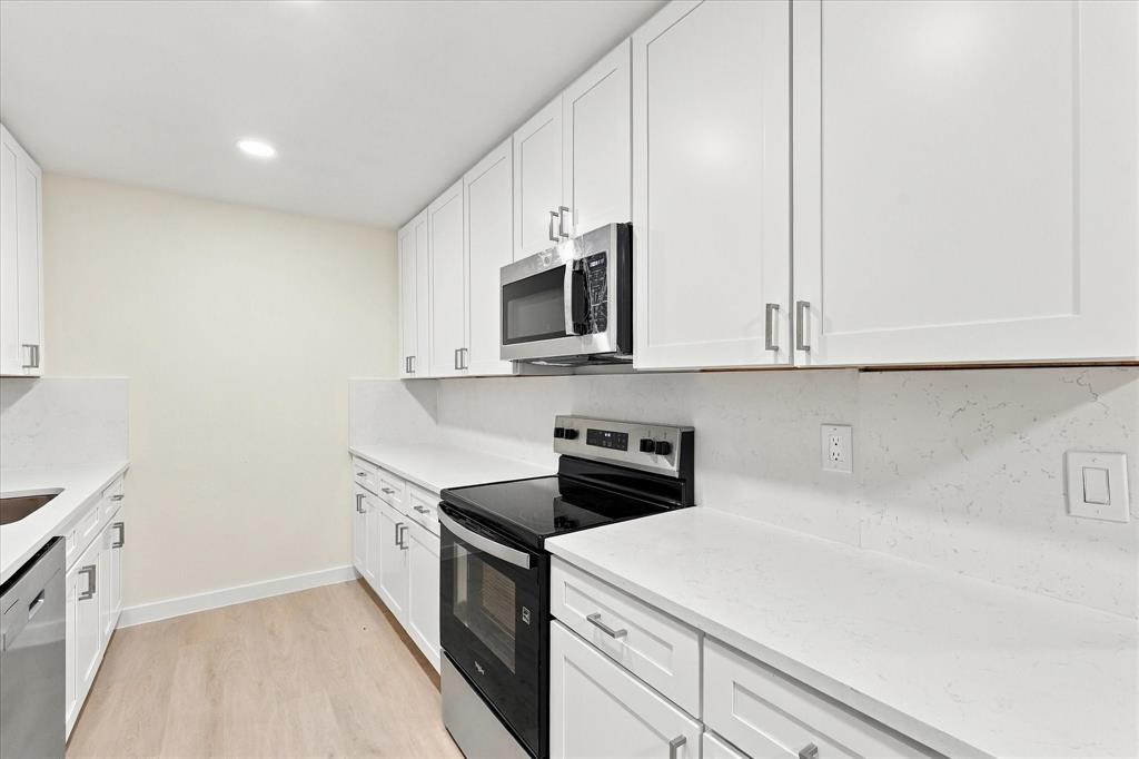 Kitchen featuring white shaker-style cabinetry, solid-surface countertops, matching slab backsplash, stainless steel appliances, and wood-finish flooring
