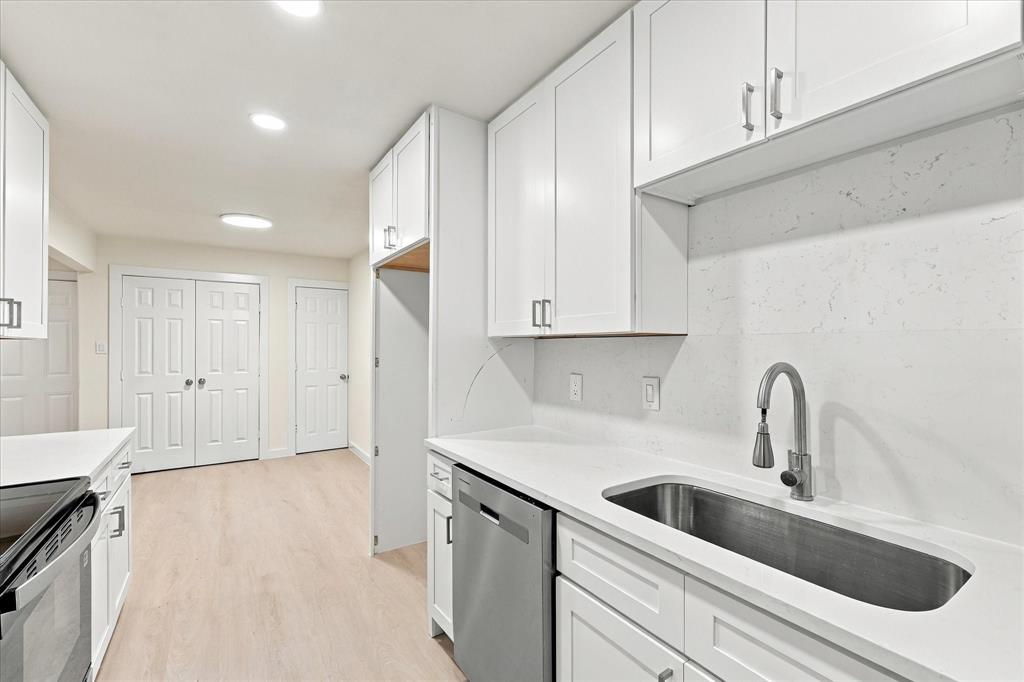 White cabinetry with clean-line hardware, solid-surface countertops, full-height slab backsplash, stainless steel sink with pull-down faucet, and recessed lighting
