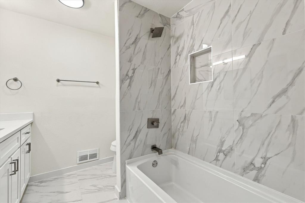 Bathroom featuring large-format veined tile surround, recessed wall niche, soaking tub, vanity with solid-surface countertop, and matte black fixtures