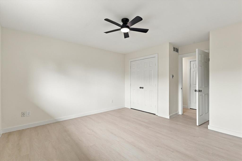 Neutral interior space featuring wood-finish flooring, a matte black ceiling fan with integrated lighting, and white six-panel doors