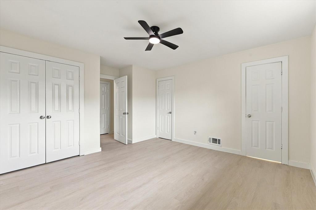 Room featuring wood-finish flooring, a central ceiling fan with integrated lighting, and multiple six-panel interior doors