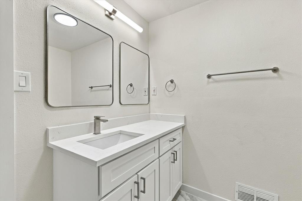 White vanity featuring a solid surface countertop, rectangular under-mount sink, brushed-nickel hardware, dual wall-mounted mirrors, and linear overhead lighting