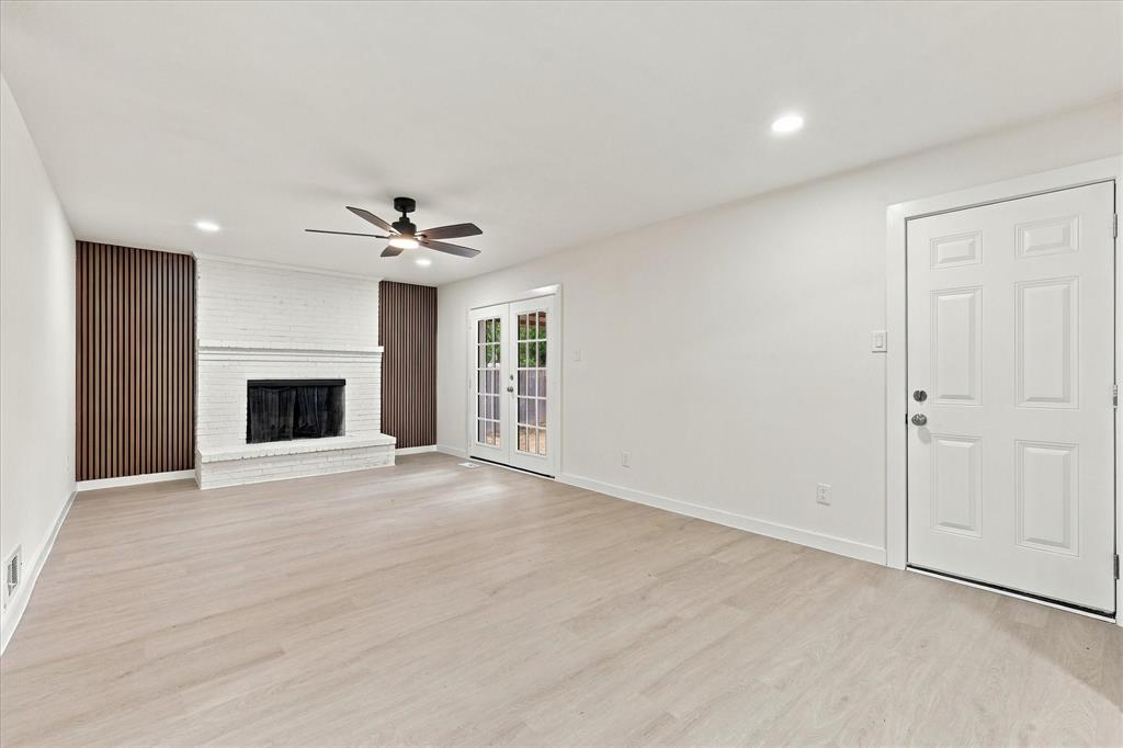 Interior space featuring light wood-finish flooring, a white brick fireplace with vertical slat accent walls, a ceiling fan, and French doors