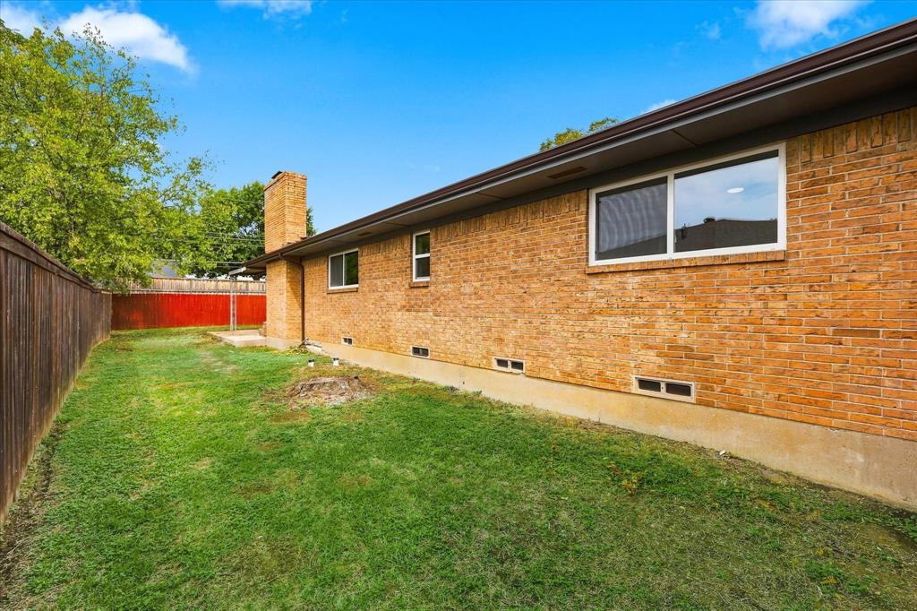 Exterior brick facade featuring a masonry chimney, horizontal sliding windows, and a fenced backyard