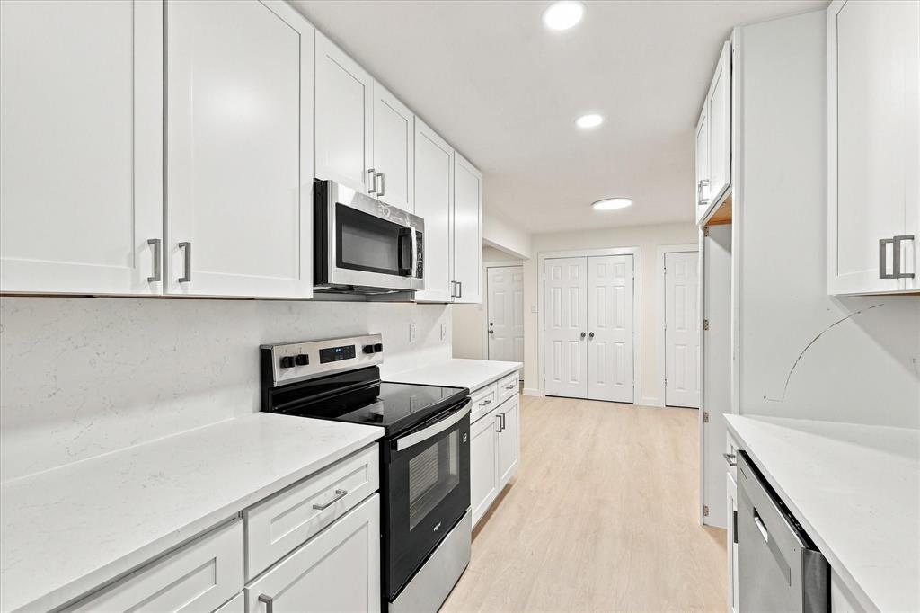 Kitchen featuring white shaker-style cabinetry, solid-surface countertops, recessed lighting, and stainless steel appliances