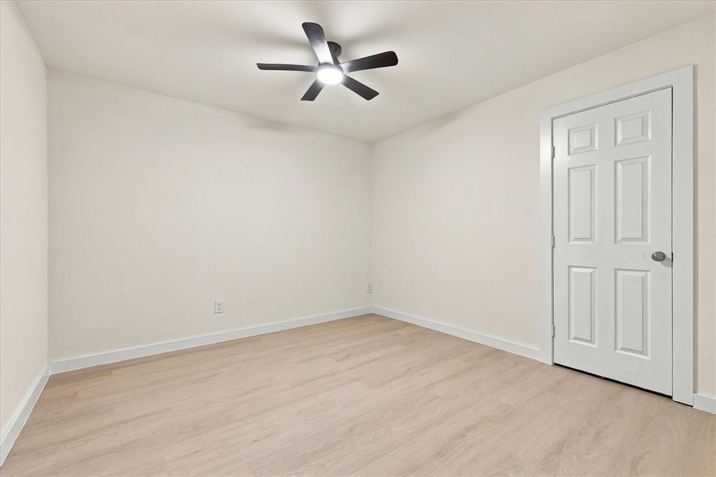 Neutral-toned interior space featuring light wood-finish flooring, a six-panel interior door, and a five-blade ceiling fan with integrated lighting