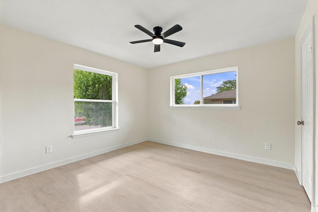 Neutral-toned interior space featuring light wood-finish flooring, two large windows, and a matte black ceiling fan with an integrated light fixture