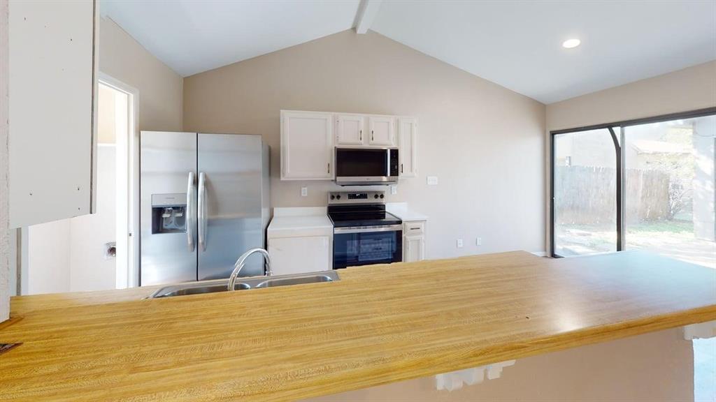 Kitchen featuring a vaulted ceiling, wood-finish breakfast bar, stainless steel appliances, white cabinetry, and sliding glass doors Kitchen featuring a vaulted ceiling, wood-finish breakfast bar, stainless steel appliances, white cabinetry, and sliding glass doors