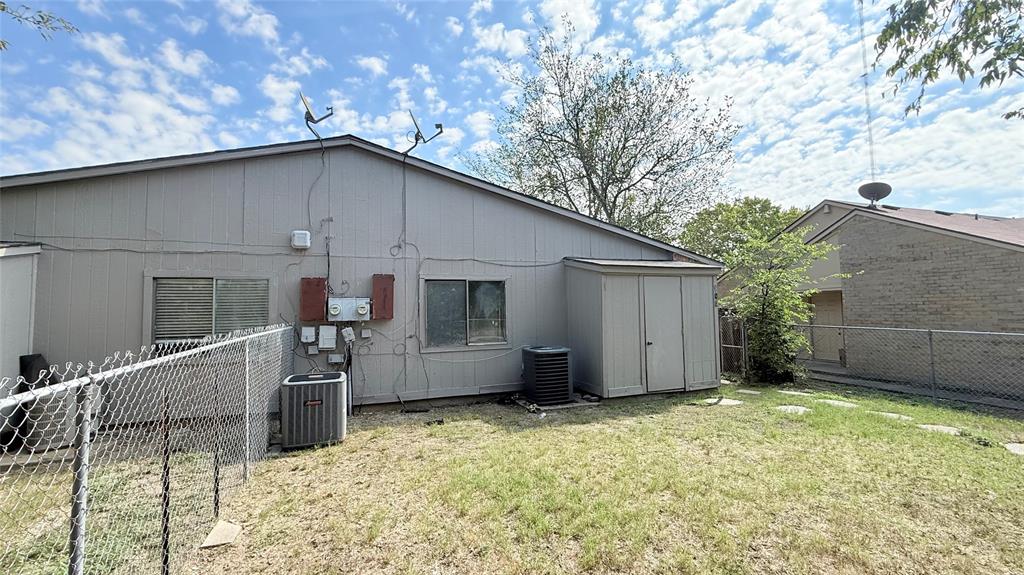 Exterior elevation featuring vertical panel siding, metal chain-link fencing, built-in outdoor storage shed, and external HVAC units