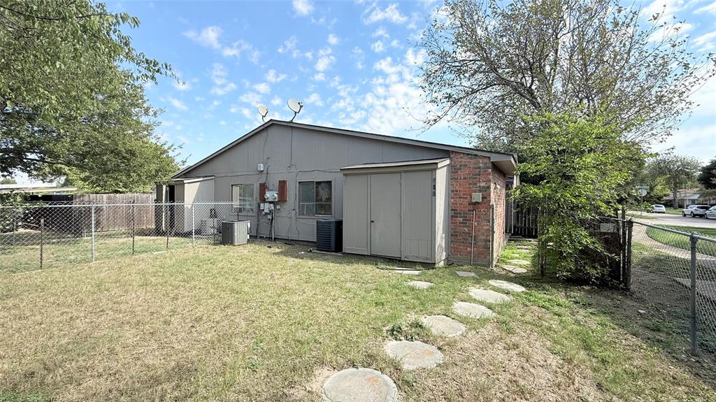 Exterior featuring brick masonry, horizontal siding, attached storage shed, chain-link fencing, and stone paver walkway