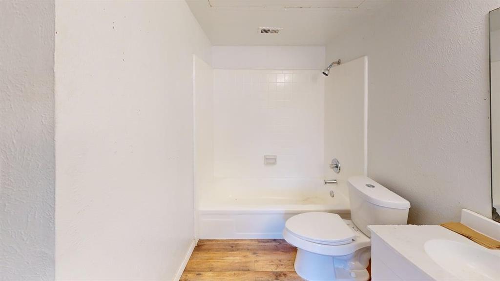 Bathroom featuring wood-finish flooring, white tub-shower combination with tiled surround, and vanity with integrated basin