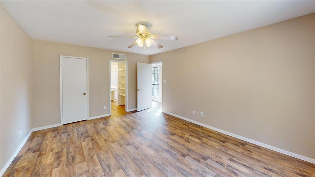 Neutral interior featuring wood-finish flooring, a multi-blade ceiling fan with integrated light fixture, and an built-in closet with shelving Neutral interior featuring wood-finish flooring, a multi-blade ceiling fan with integrated light fixture, and an built-in closet with shelving