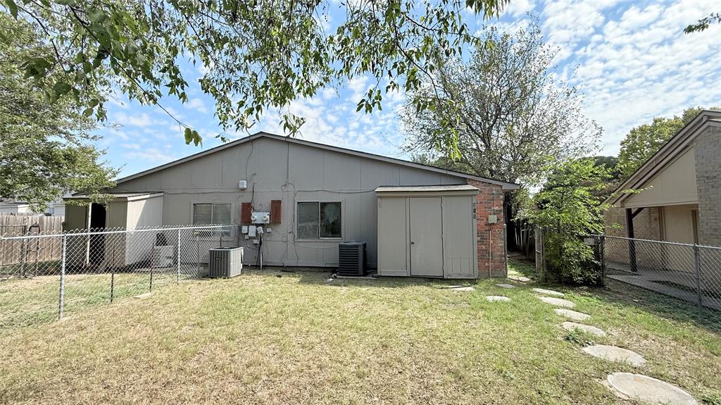 Rear exterior featuring vertical siding, brick accents, integrated storage structures, and a chain-link fenced yard with a stone path