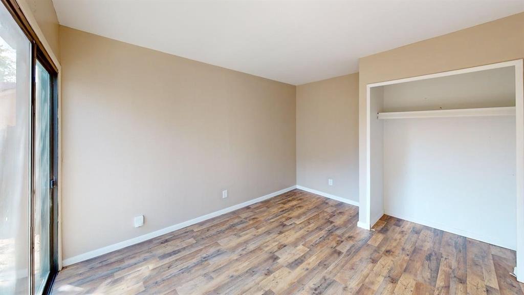 Room featuring wood-finish flooring, neutral wall paint, and a sliding glass door providing exterior access, plus a built-in closet with an integrated shelf