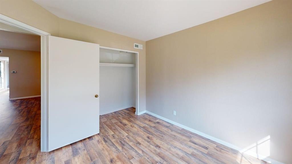 Neutral-toned interior space featuring wood-finish flooring and a built-in closet with an integrated shelving rod Neutral-toned interior space featuring wood-finish flooring and a built-in closet with an integrated shelving rod