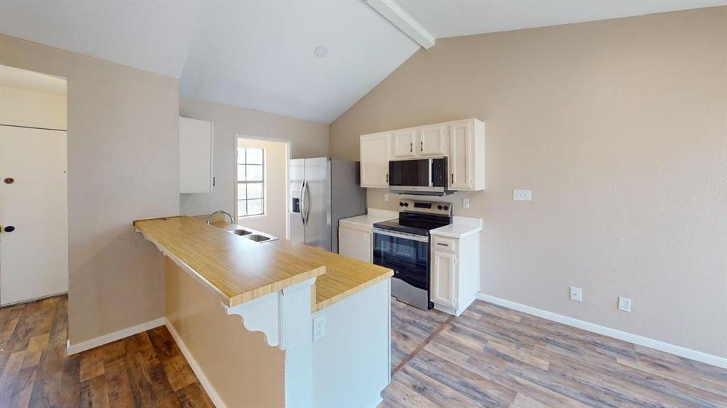 Kitchen featuring white cabinetry, wood-finish countertop, stainless steel appliance package, and vaulted ceiling with wood-finish flooring Kitchen featuring white cabinetry, wood-finish countertop, stainless steel appliance package, and vaulted ceiling with wood-finish flooring