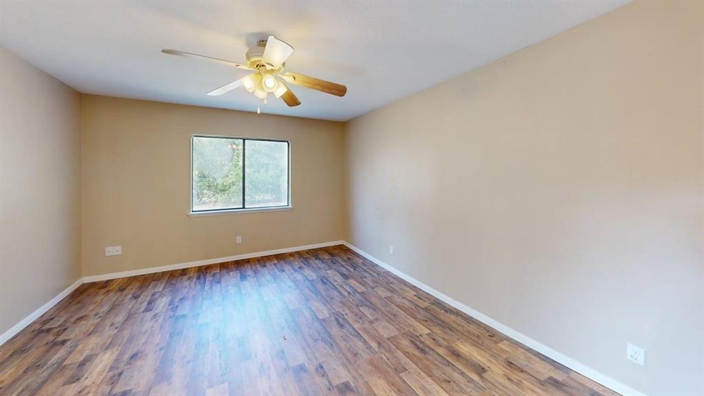 Room featuring wood-finish flooring, a multi-blade ceiling fan with integrated lighting, and a window with a natural exterior backdrop Room featuring wood-finish flooring, a multi-blade ceiling fan with integrated lighting, and a window with a natural exterior backdrop
