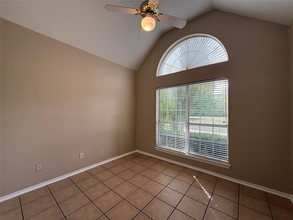 Vaulted ceilings, arched window featuring a sunburst design, tile flooring, and a ceiling fan with integrated lighting