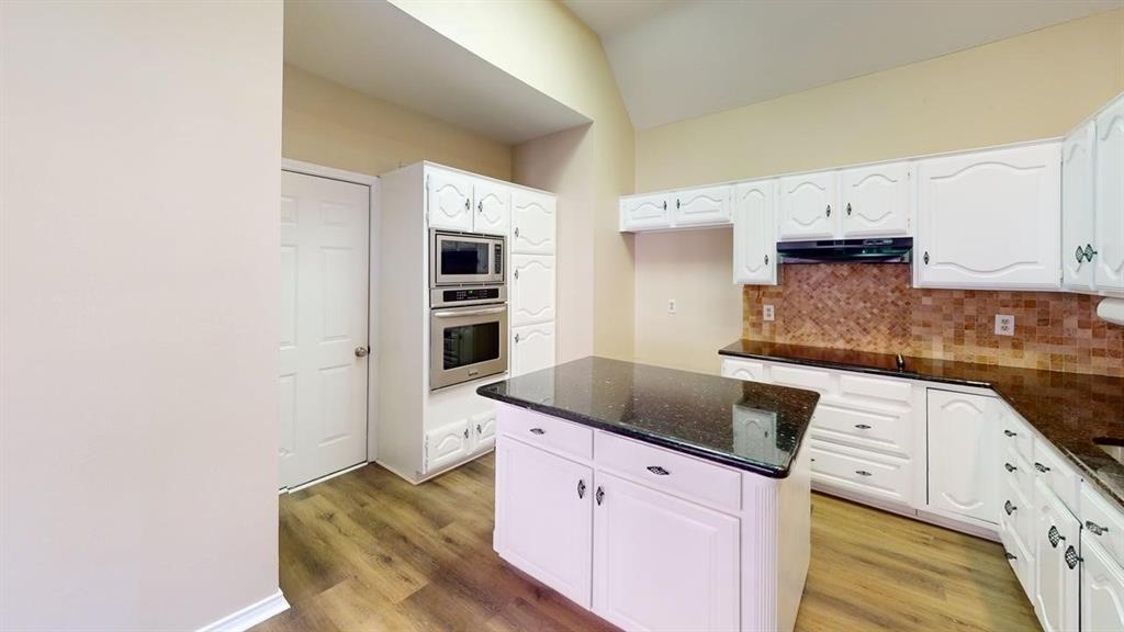 Kitchen featuring a vaulted ceiling, wood-finish flooring, white cabinetry, dark stone countertops, and a built-in double oven