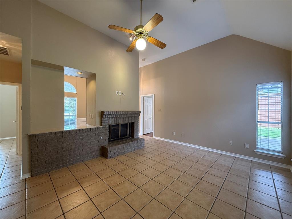 Vaulted ceiling, brick fireplace with a raised hearth, and tile flooring