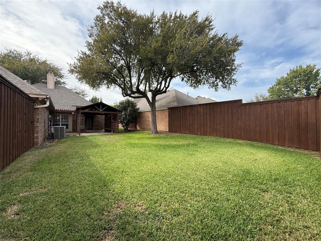 Backyard featuring a grass lawn, mature tree, wood privacy fencing, and a covered patio area
