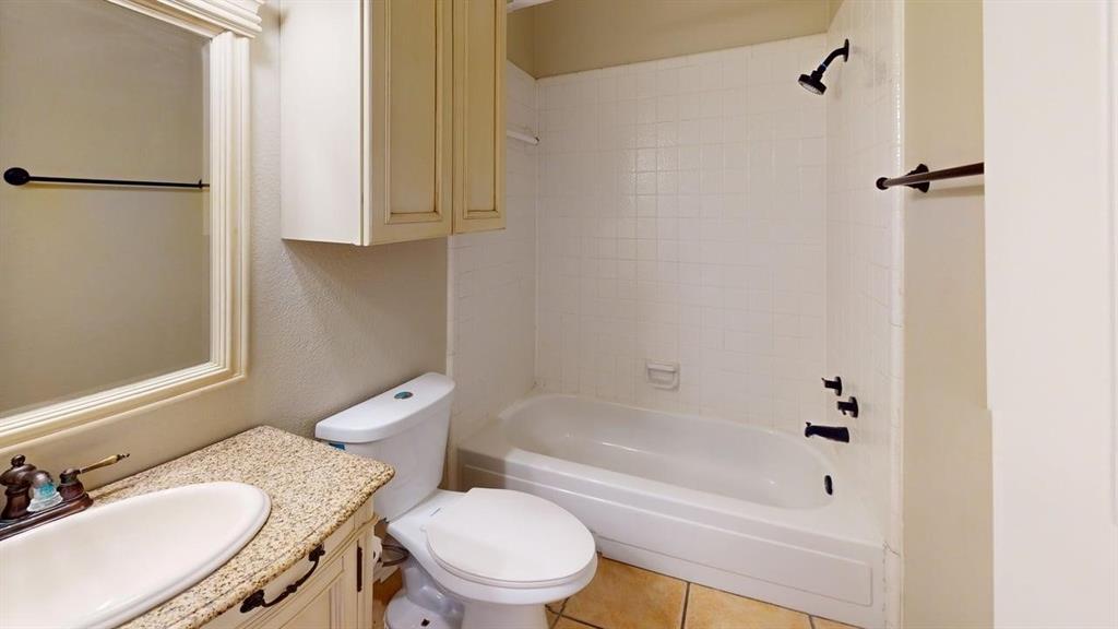 Bathroom featuring a stone-composite countertop with an integrated oval basin, light-toned built-in cabinetry, tile-surround shower and tub combination, and matte black hardware