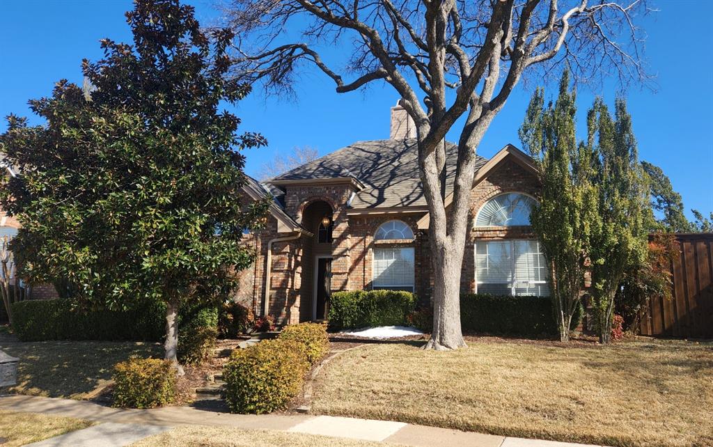 Brick exterior featuring an arched entryway, stone detailing, arched windows, and mature landscaping