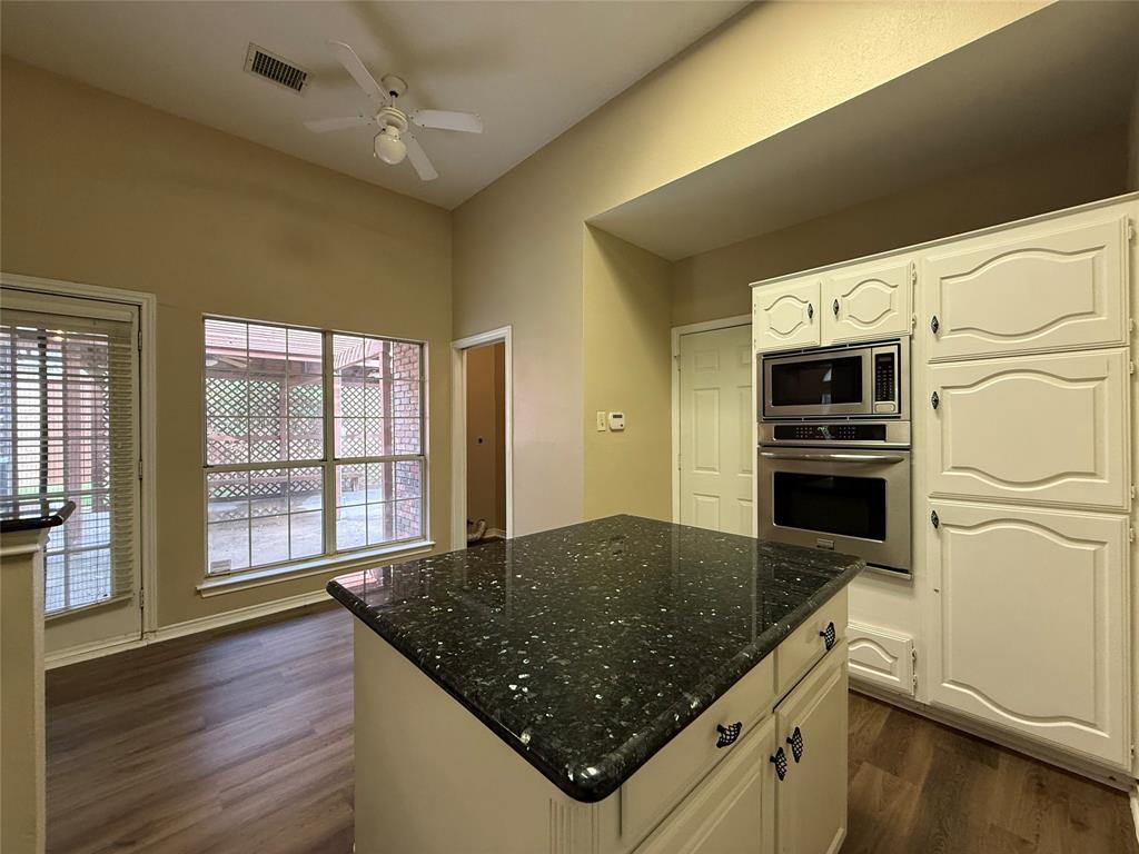 Kitchen area featuring a central island with a dark stone countertop, built-in stainless steel double wall ovens, white cabinetry, wood-finish flooring, and a vaulted ceiling