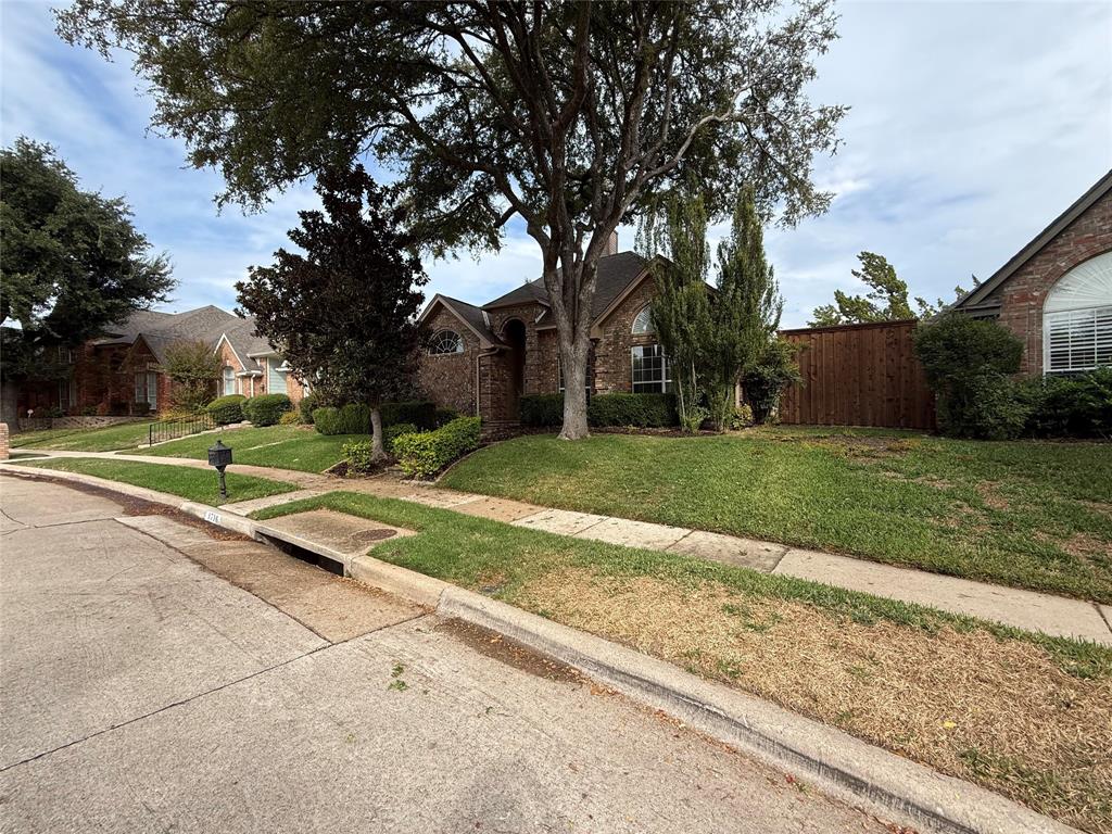 Brick exterior facade with arched window detailing, mature shade trees, and a wood privacy fence