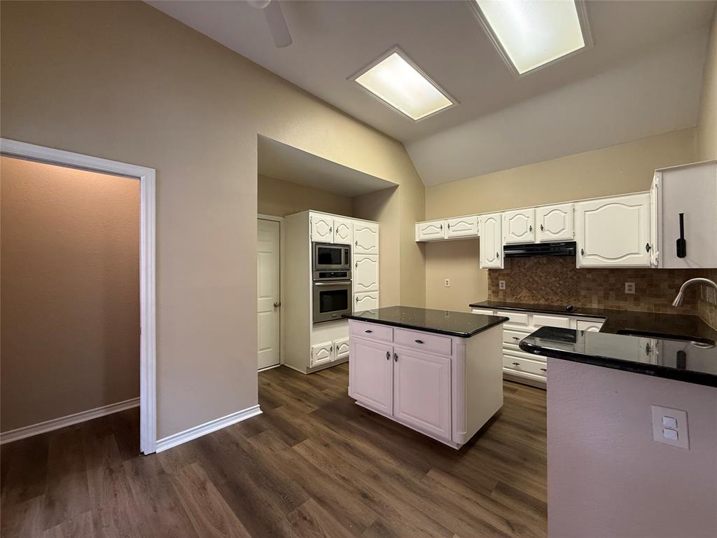 Kitchen featuring vaulted ceilings, recessed lighting, wood-finish flooring, a central island with a stone-finish countertop, and integrated double wall ovens