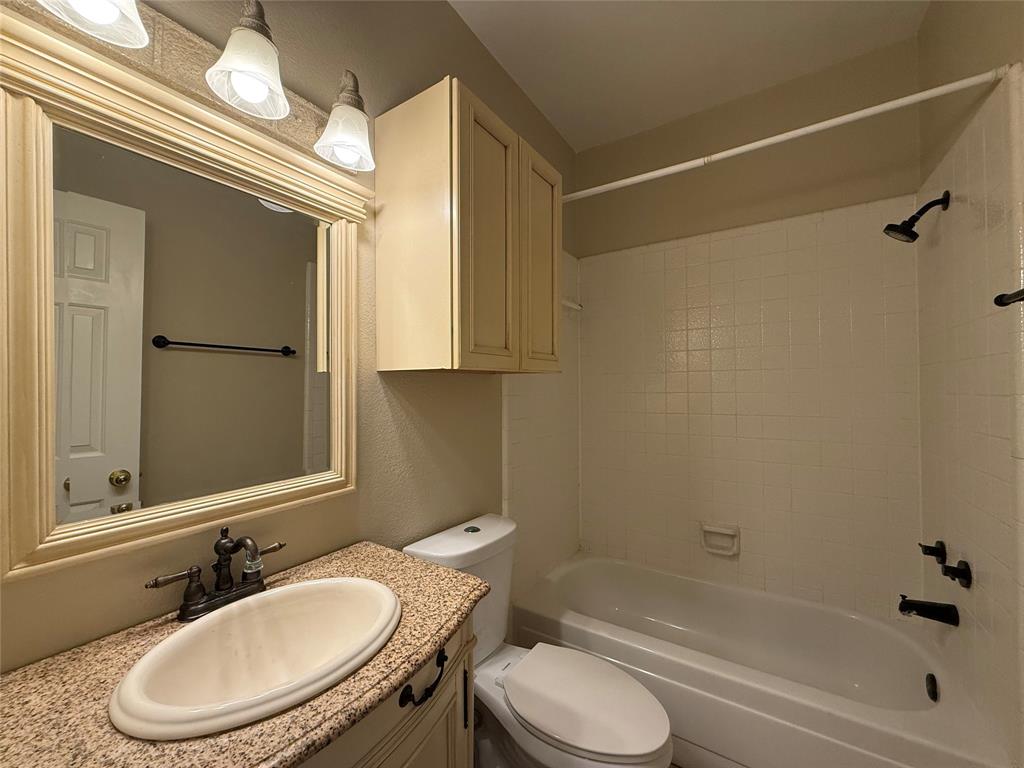 Bathroom featuring a vanity with a speckled countertop, oval undermount sink, three-light fixture, built-in cabinetry, and a shower-tub combination with tiled surround