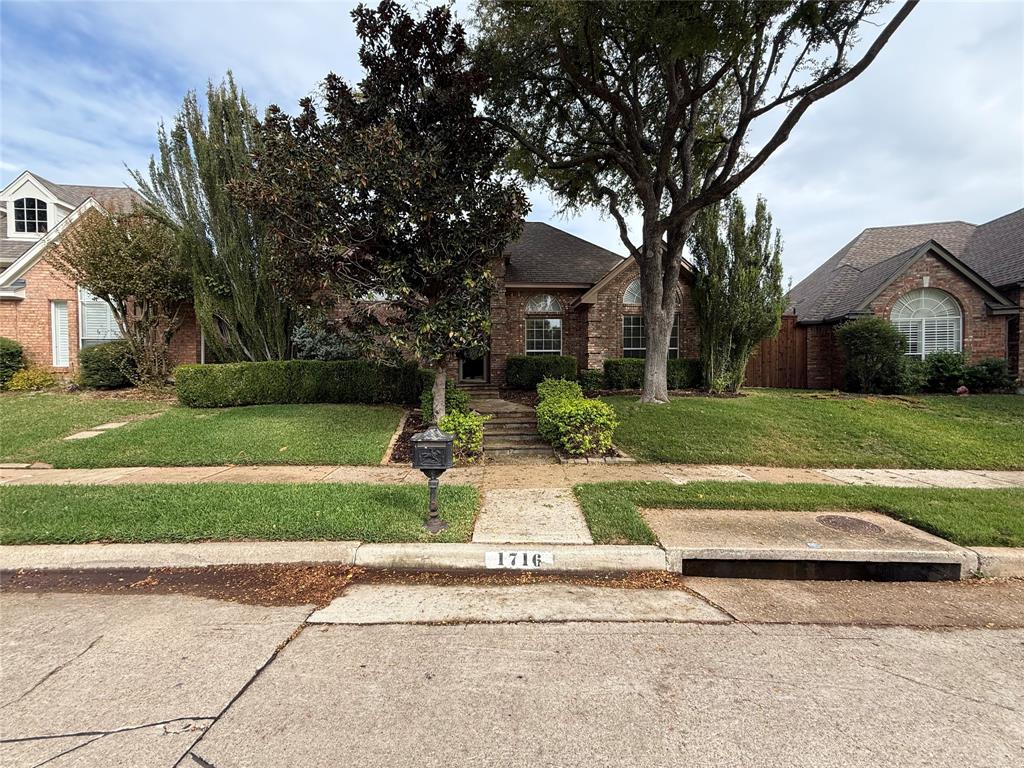 Brick exterior residence featuring a gabled roofline, arched windows, and mature landscaping