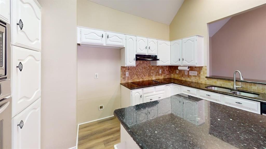 Kitchen featuring white cabinetry, dark stone countertops, wood-finish flooring, a vaulted ceiling, and a stainless steel undermount sink with a gooseneck faucet