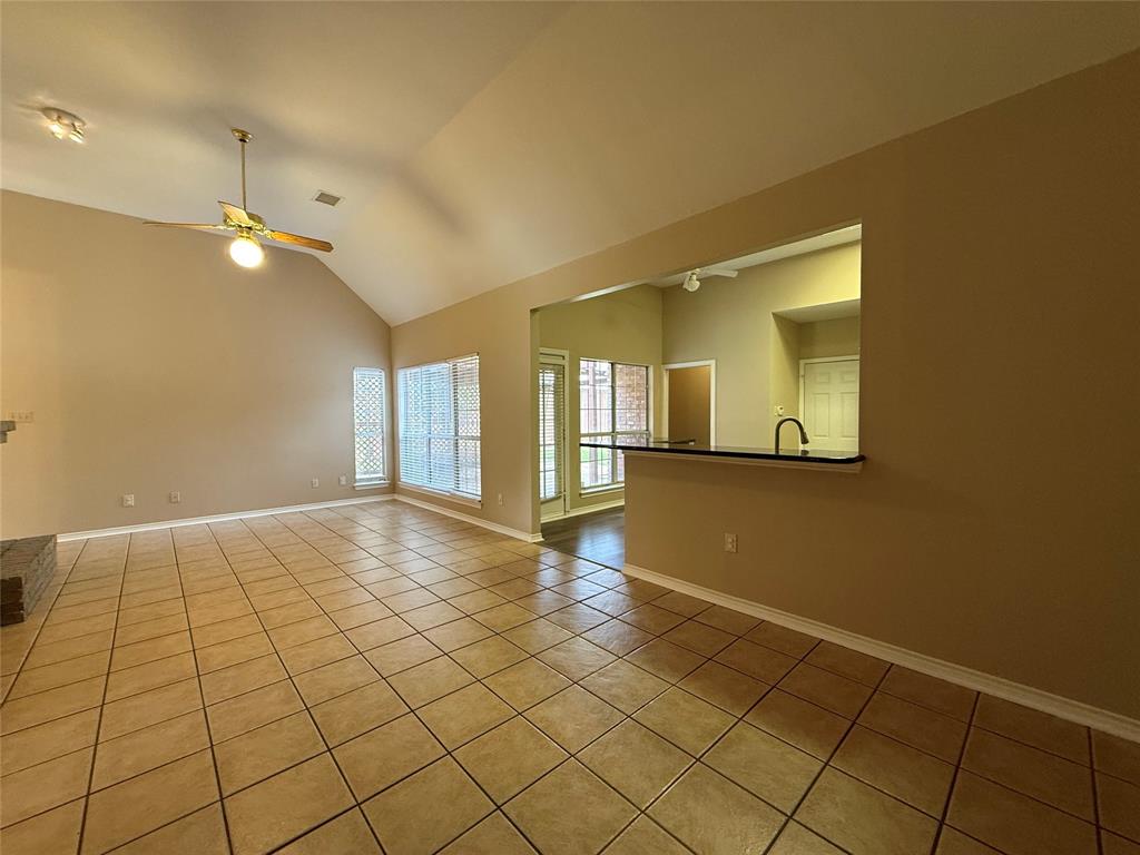 Vaulted ceilings featuring a central ceiling fan, neutral wall finishes, tile flooring, large windows, and a pass-through bar with a countertop