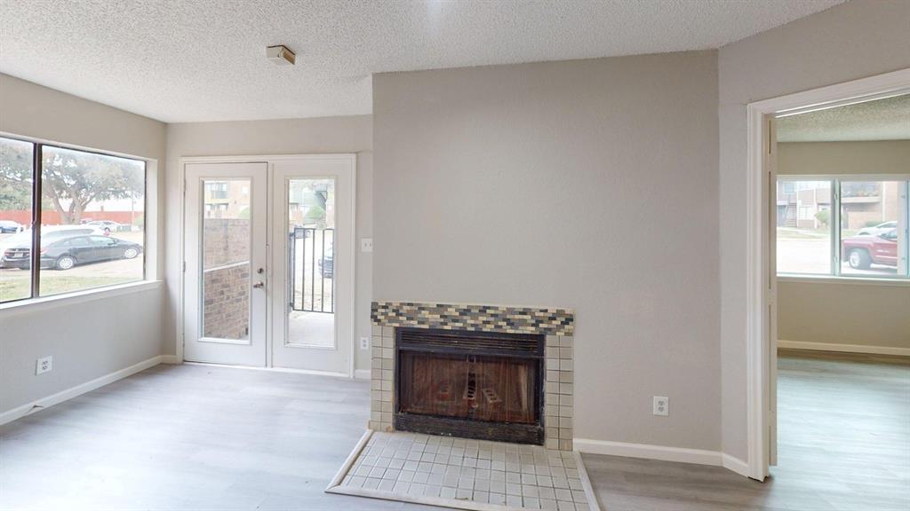 Fireplace with tile surround and stone-patterned accents, light-toned wood-finish flooring, glass-paned exterior door, and large windows providing natural light