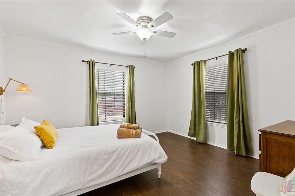 Room featuring dark wood-finish flooring, two dual-pane windows with horizontal blinds, a ceiling fan with integrated lighting, and a wall-mounted swing-arm light fixture