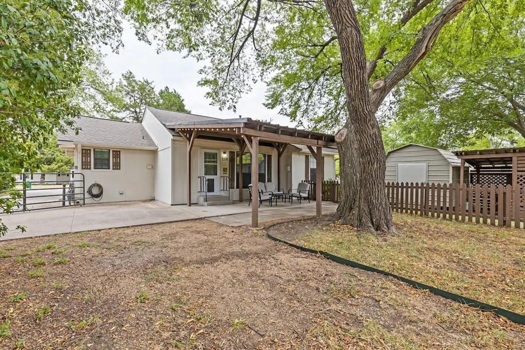 Covered wooden pergola, concrete patio, detached storage shed, and mature trees situated on a fenced lot