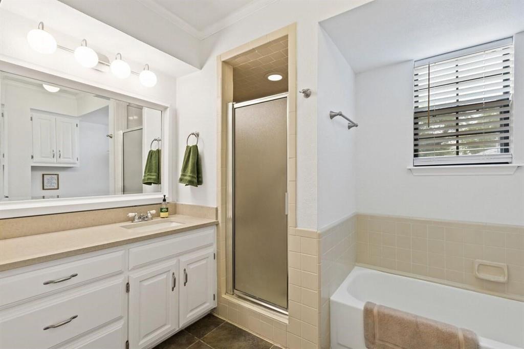 Bathroom featuring white cabinetry, solid-surface countertop with integrated sink, glass-enclosed shower, tiled bathtub surround, and wall-mounted light fixture