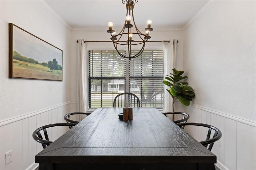 Dining area featuring vertical wainscoting, crown molding, and a central iron chandelier Dining area featuring vertical wainscoting, crown molding, and a central iron chandelier